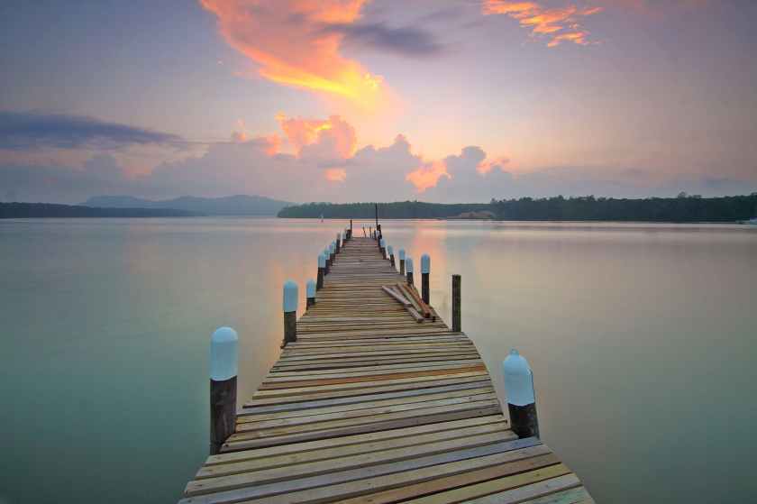 brown wooden footbridge on body of water during sunrise